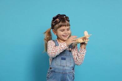 Happy little girl playing with toy plane on light blue background