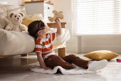 Photo of Cute little boy in aviator goggles playing with toy plane at home