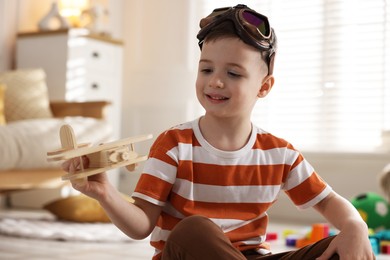 Photo of Happy little boy playing with toy plane at home