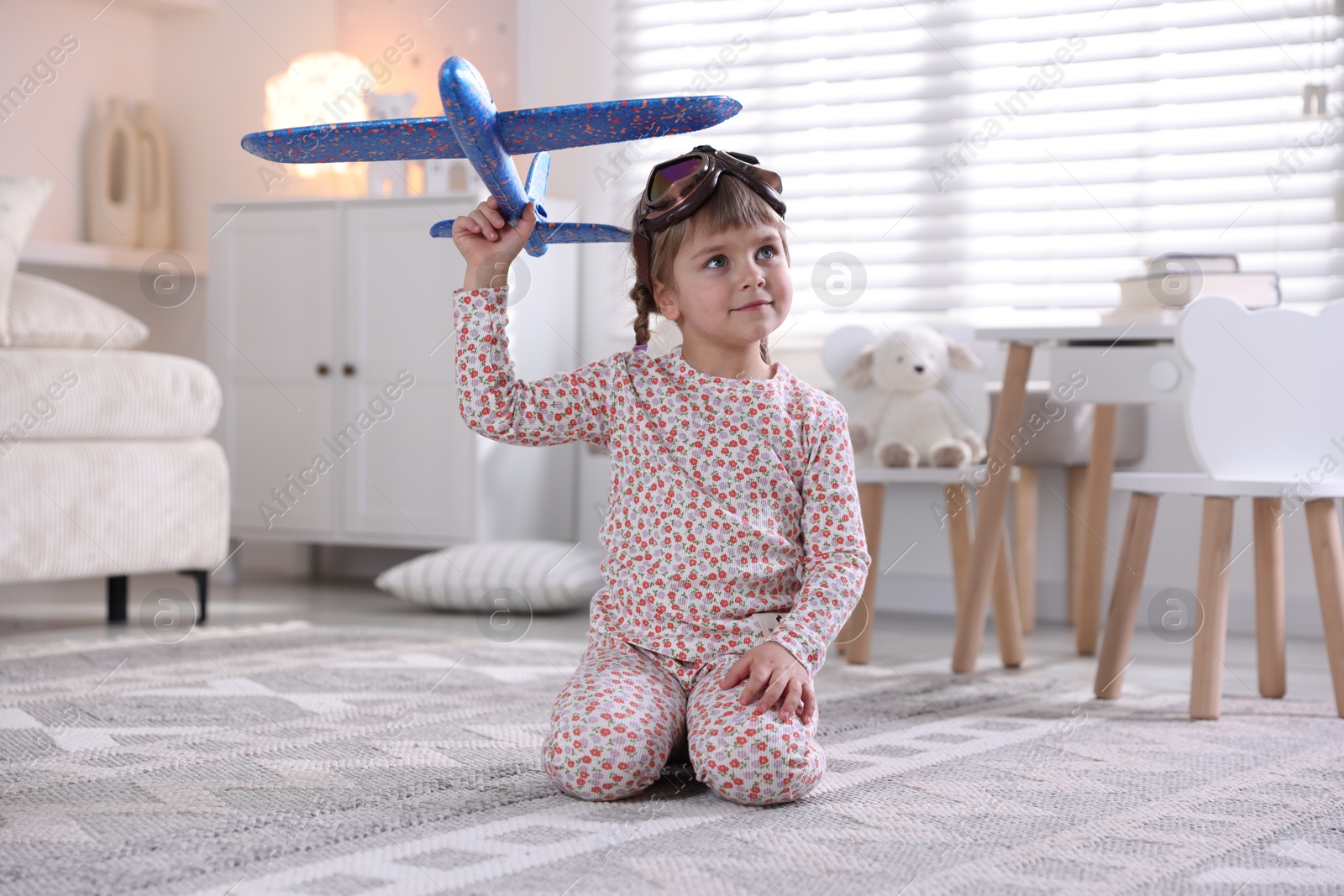 Photo of Cute little girl playing with toy plane at home