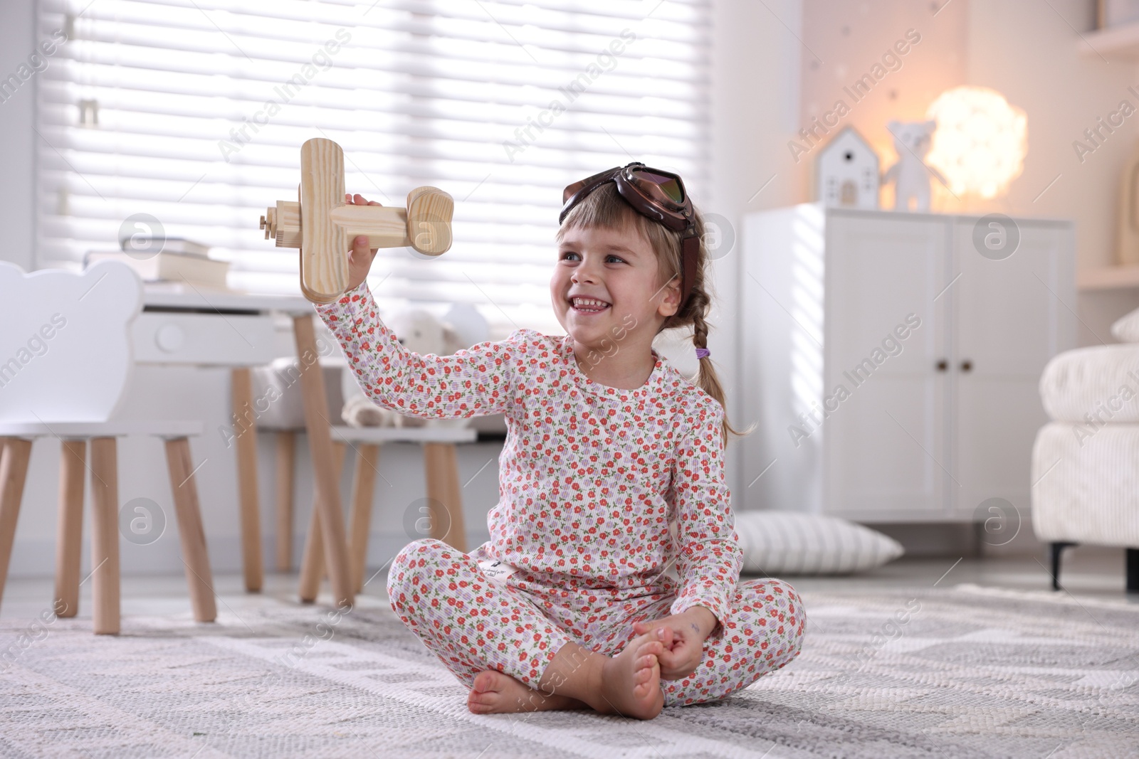 Photo of Cute little girl playing with toy plane at home