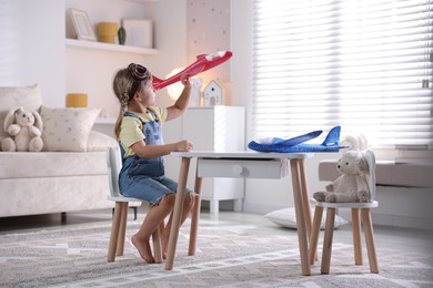 Photo of Cute little girl playing with toy plane at home