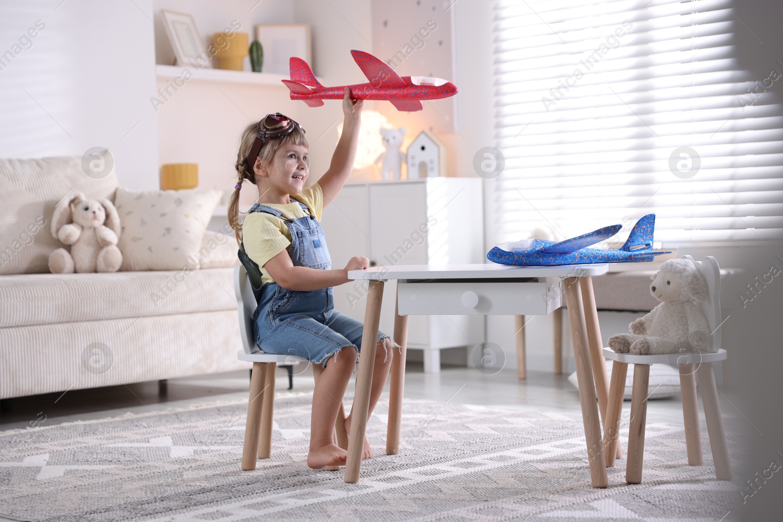 Photo of Cute little girl playing with toy plane at home