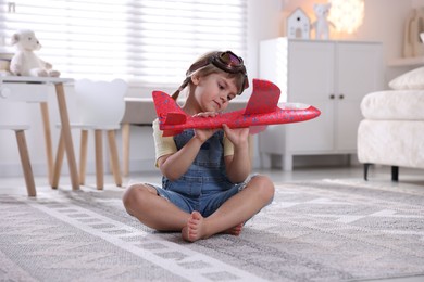 Photo of Cute little girl playing with toy plane at home