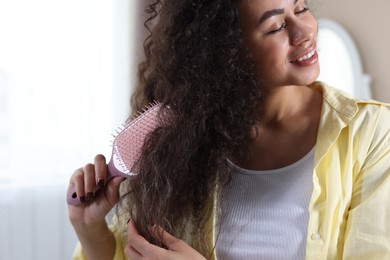 Photo of Young woman brushing her curly hair indoors