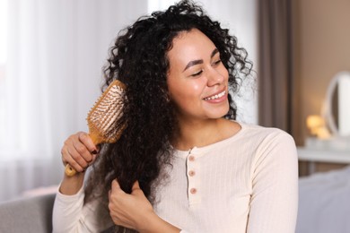 Photo of Smiling young woman brushing her curly hair at home