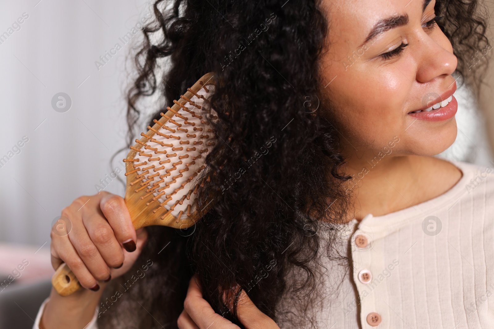 Photo of Smiling young woman brushing her curly hair indoors, closeup