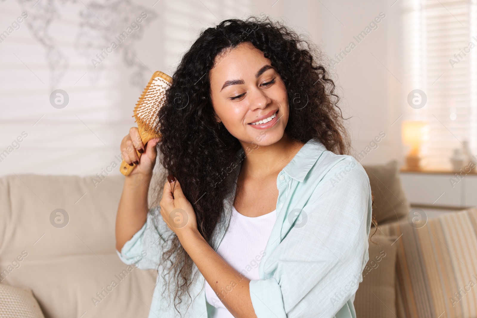 Photo of Smiling young woman brushing her curly hair at home