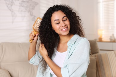 Photo of Smiling young woman brushing her curly hair at home