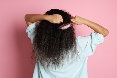 Photo of Woman brushing her curly hair on pink background, back view