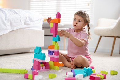 Photo of Cute little girl playing with colorful building blocks on floor at home