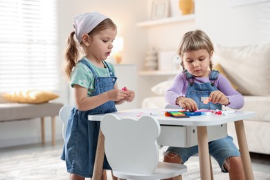 Cute little sisters drawing at white table in room