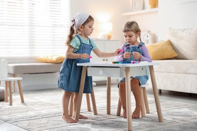 Cute little sisters drawing at white table in room