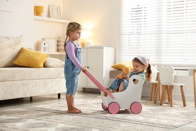 Photo of Cute little sisters playing with toy stroller at home