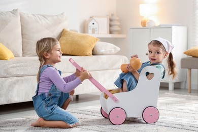 Cute little sisters playing with toy stroller at home