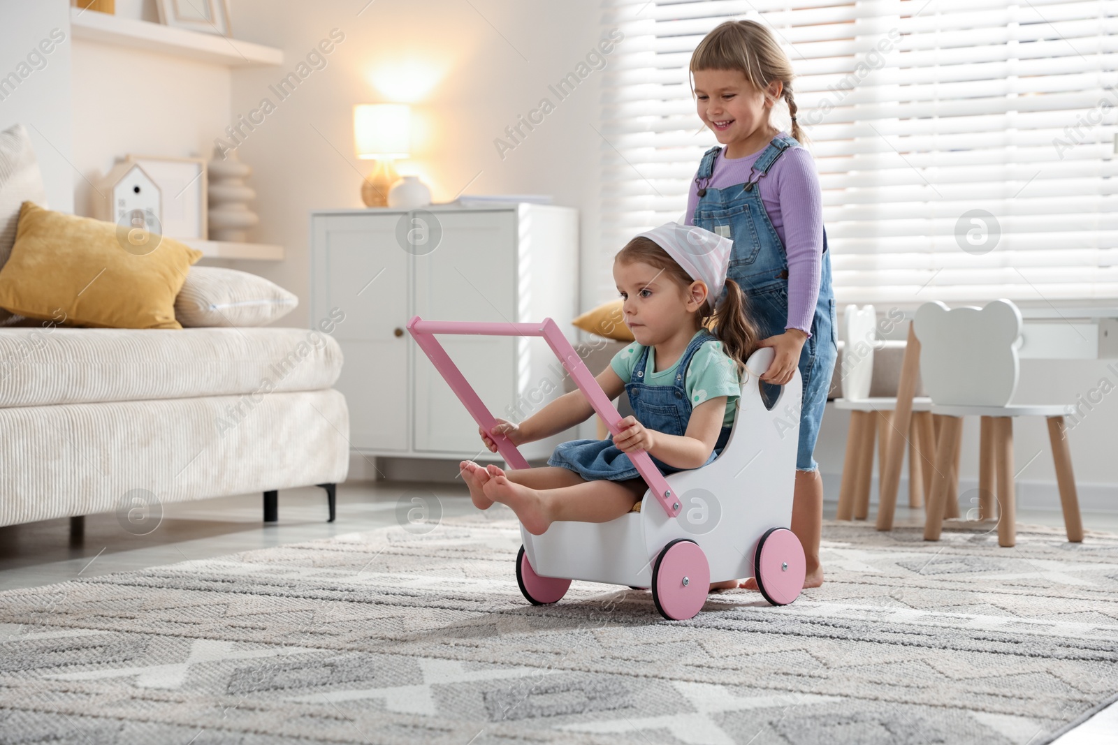 Photo of Cute little sisters playing with toy stroller at home