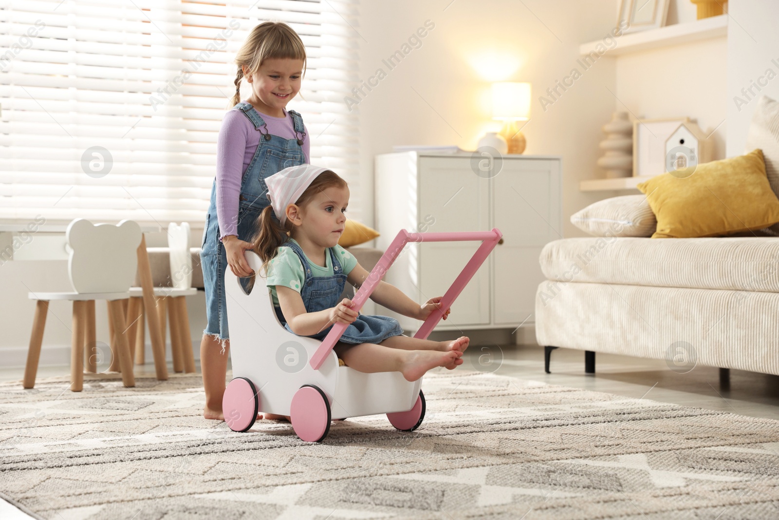 Photo of Cute little sisters playing with toy stroller at home