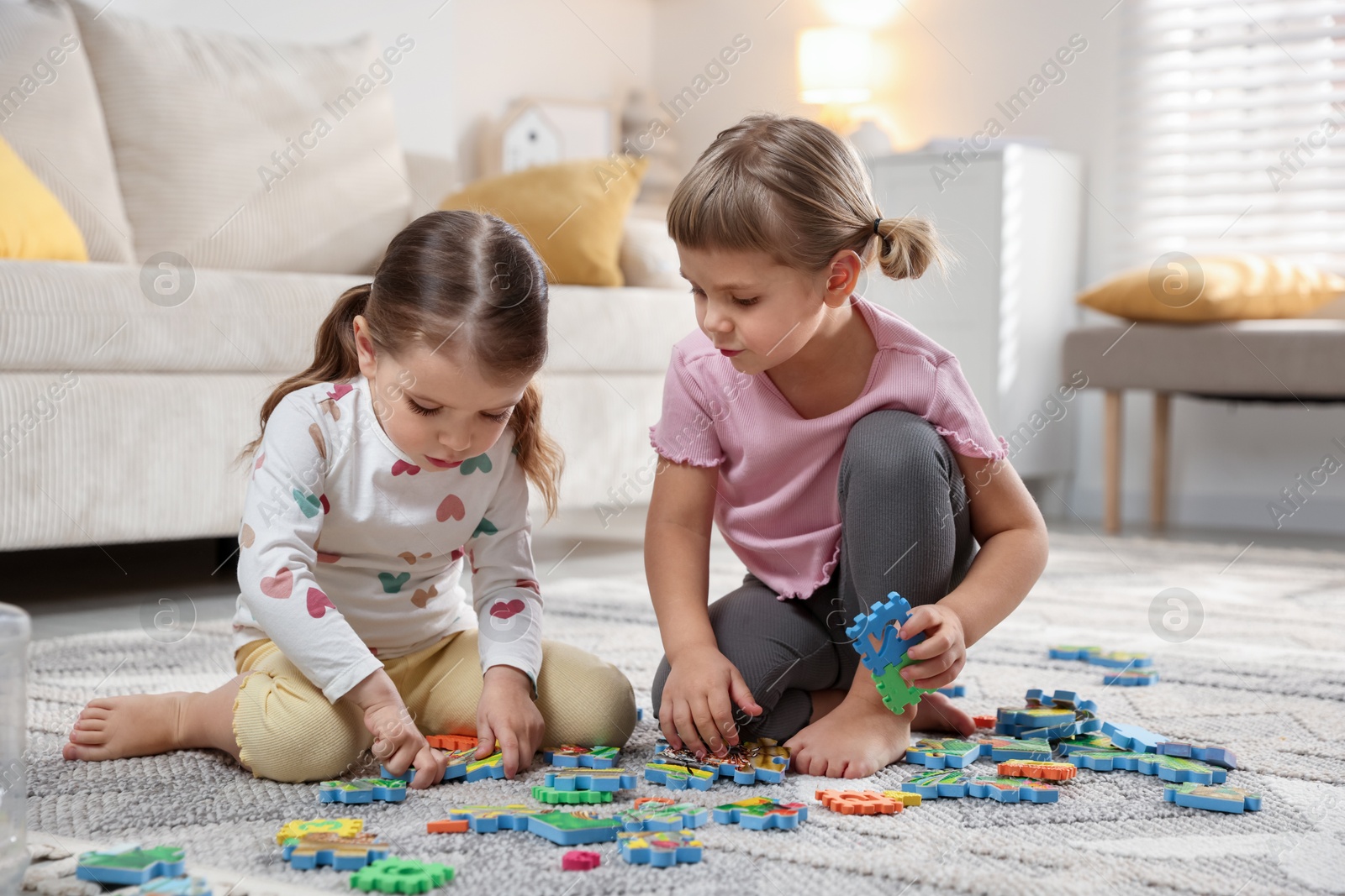 Photo of Cute little sisters playing with puzzles on floor at home