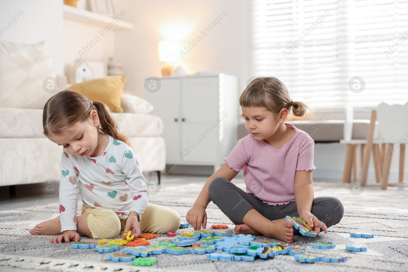 Photo of Cute little sisters playing with puzzles on floor at home