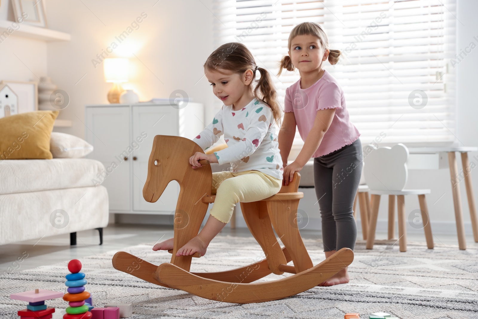 Photo of Cute little sisters playing with wooden rocking horse at home