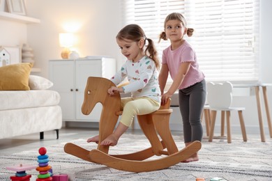 Cute little sisters playing with wooden rocking horse at home