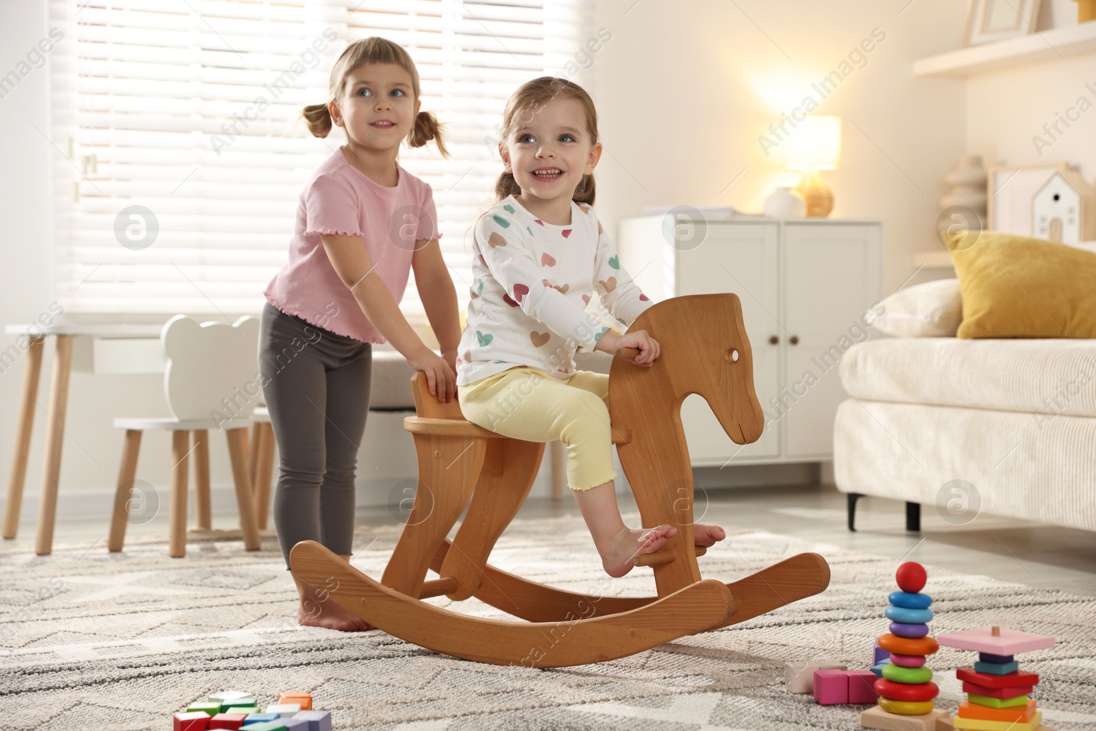 Photo of Cute little sisters playing with wooden rocking horse at home