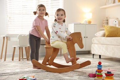 Cute little sisters playing with wooden rocking horse at home