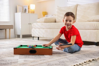 Photo of Cute little boy playing billiards at home