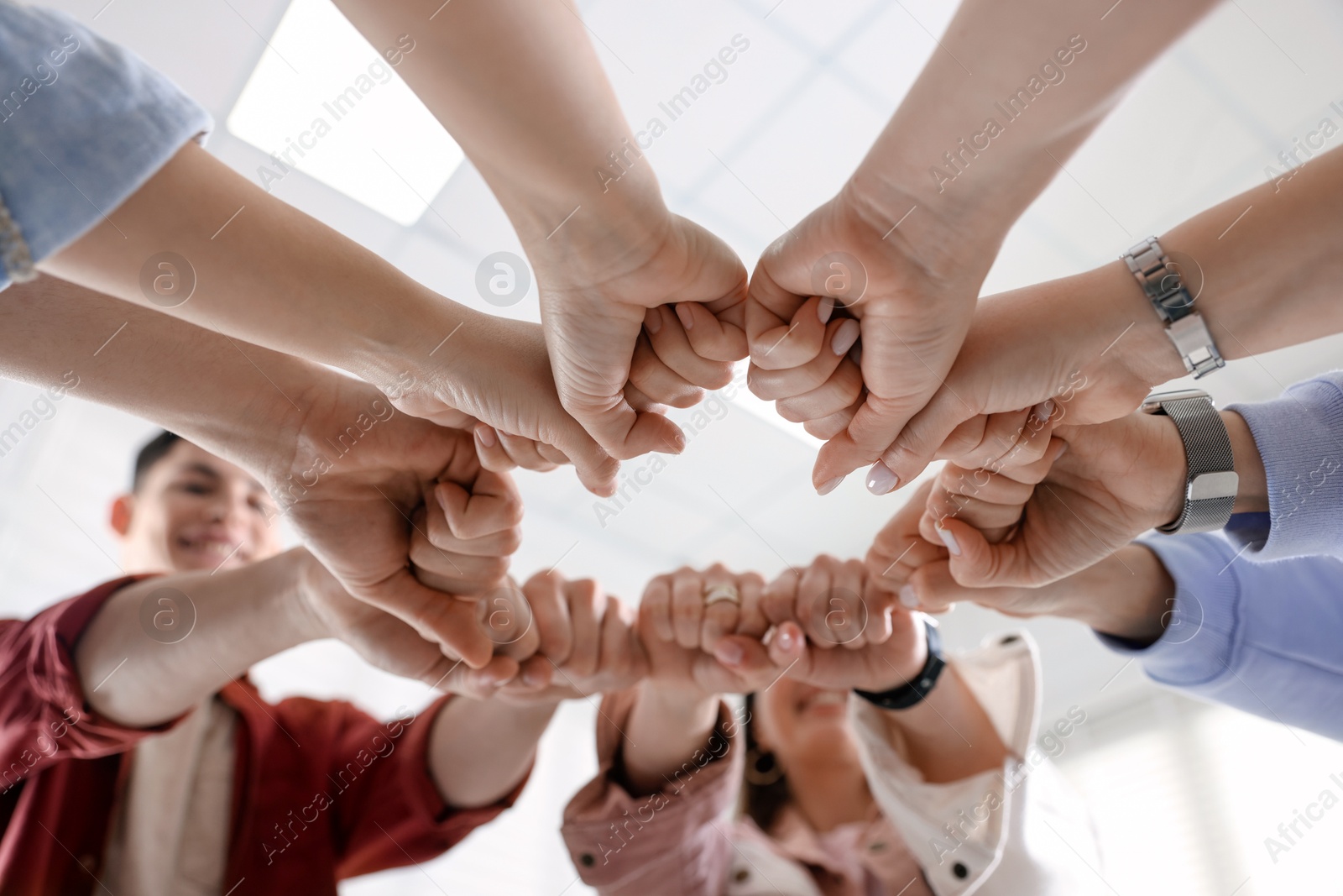 Photo of Unity concept. People holding fists together indoors, low angle view