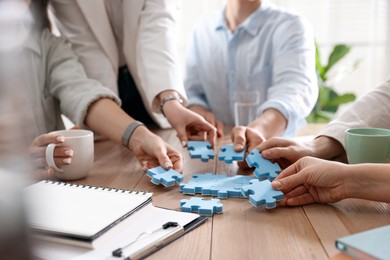 Unity concept. People putting puzzle pieces together at wooden table indoors, closeup