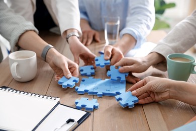 Photo of Unity concept. People putting puzzle pieces together at wooden table indoors, closeup