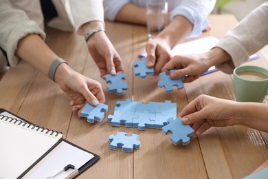 Photo of Unity concept. People putting puzzle pieces together at wooden table indoors, closeup