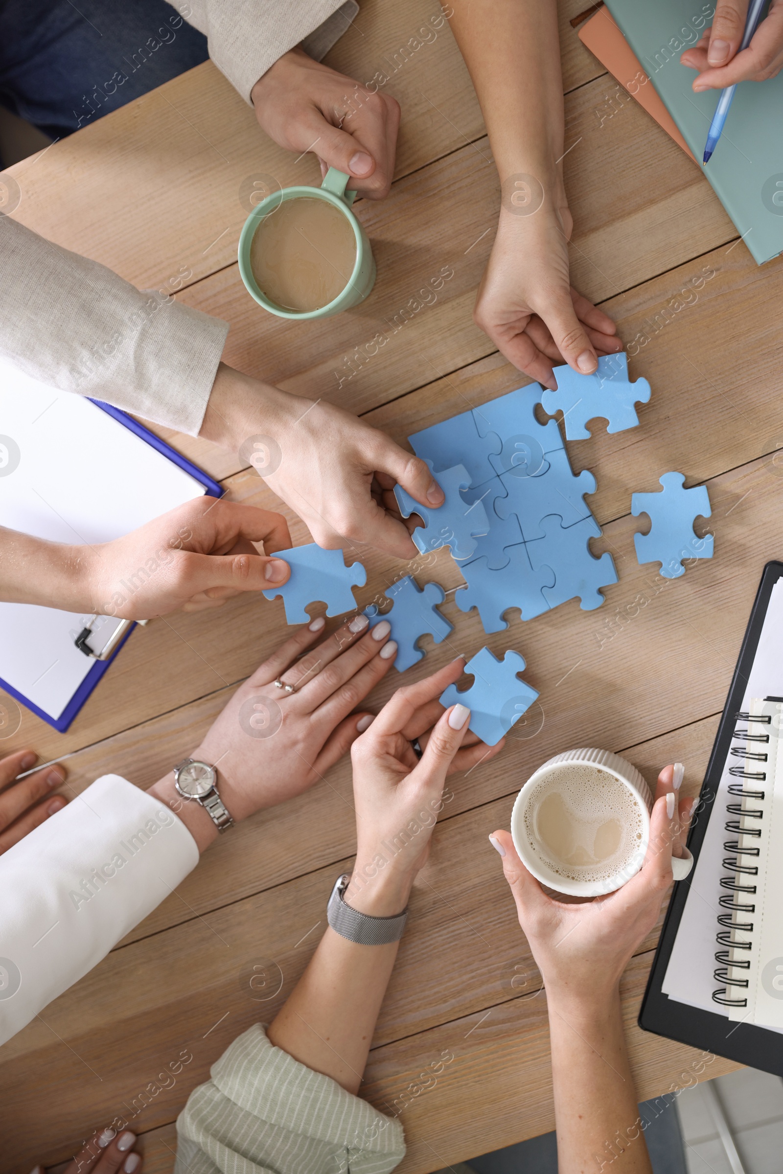 Photo of Unity concept. People putting puzzle pieces together at wooden table indoors, top view