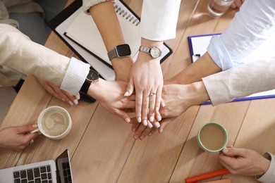 Photo of Unity concept. People holding hands together above wooden table, top view