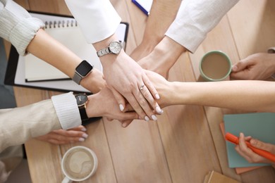 Unity concept. People holding hands together above wooden table, top view