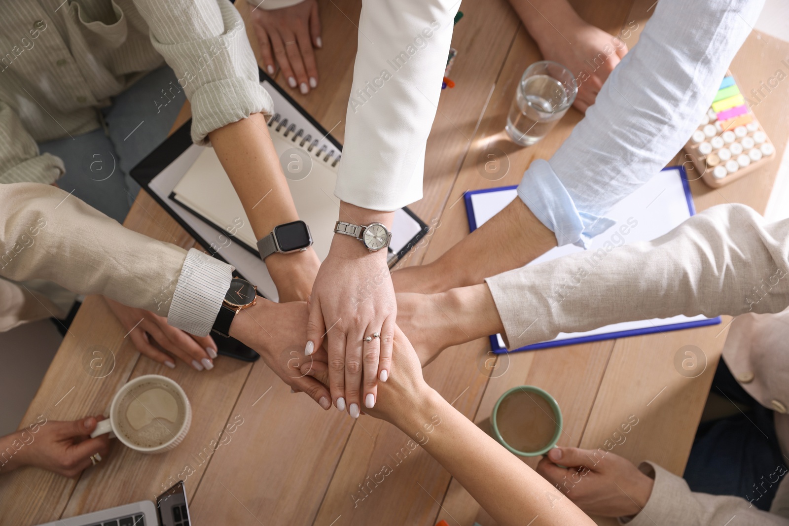 Photo of Unity concept. People holding hands together above wooden table, top view