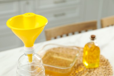 Photo of Bottle with funnel and used cooking oil on white table, closeup. Space for text