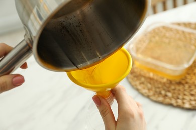 Photo of Woman pouring used cooking oil into bottle through funnel in kitchen, closeup