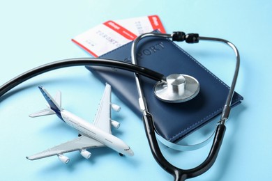 Photo of Medical tourism. Stethoscope, plane model, passport and flight tickets on light blue background, closeup