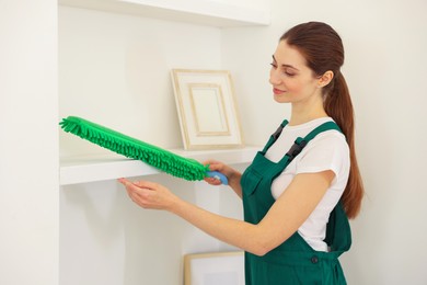 Photo of Professional janitor cleaning dust off shelves indoors