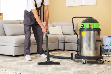 Photo of Professional cleaning service worker vacuuming rug indoors, closeup