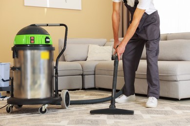 Photo of Professional cleaning service worker vacuuming rug indoors, closeup