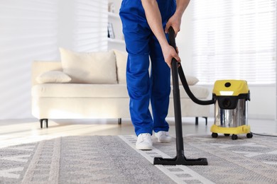 Photo of Cleaning service worker vacuuming rug with professional hoover at home, closeup