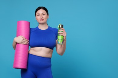 Plus size woman in gym clothes with water bottle and mat on light blue background, space for text