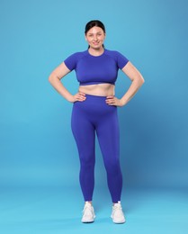 Plus size woman in gym clothes on light blue background