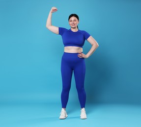 Plus size woman in gym clothes showing her bicep on light blue background, space for text