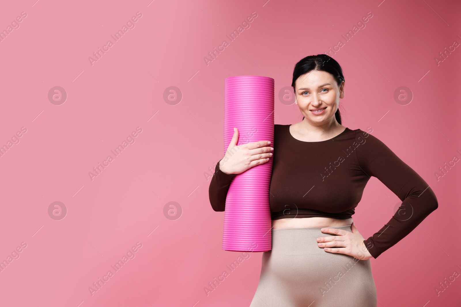 Photo of Plus size woman in gym clothes with fitness mat on pink background, space for text