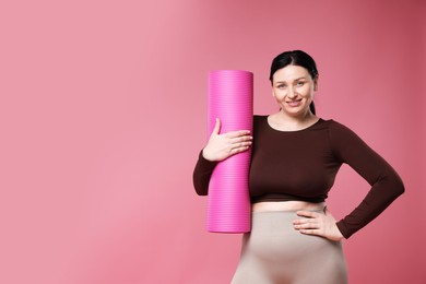 Plus size woman in gym clothes with fitness mat on pink background, space for text