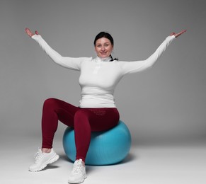 Plus size woman in gym clothes with fitness ball on grey background