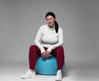 Plus size woman in gym clothes with fitness ball on grey background